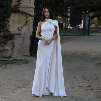 Woman in a white dress with a cape standing outdoors.