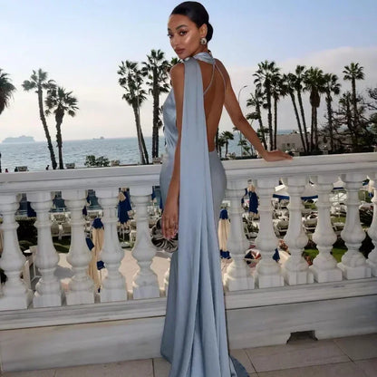 Woman in a light blue evening gown standing on a balcony with palm trees and ocean view.