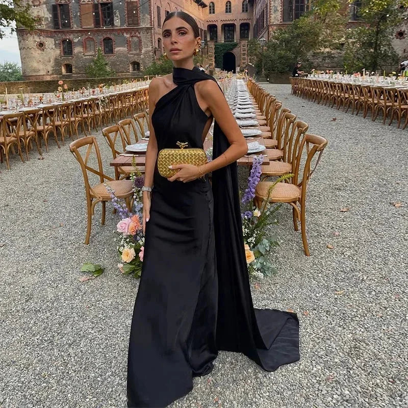 Woman in a black dress standing in front of an outdoor dining setup with tables and chairs.