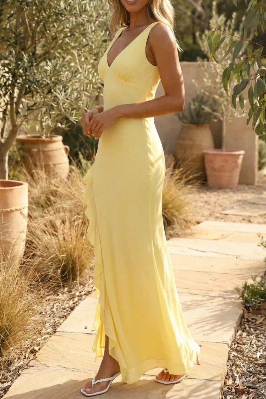 Woman in a yellow dress standing outdoors among potted plants.