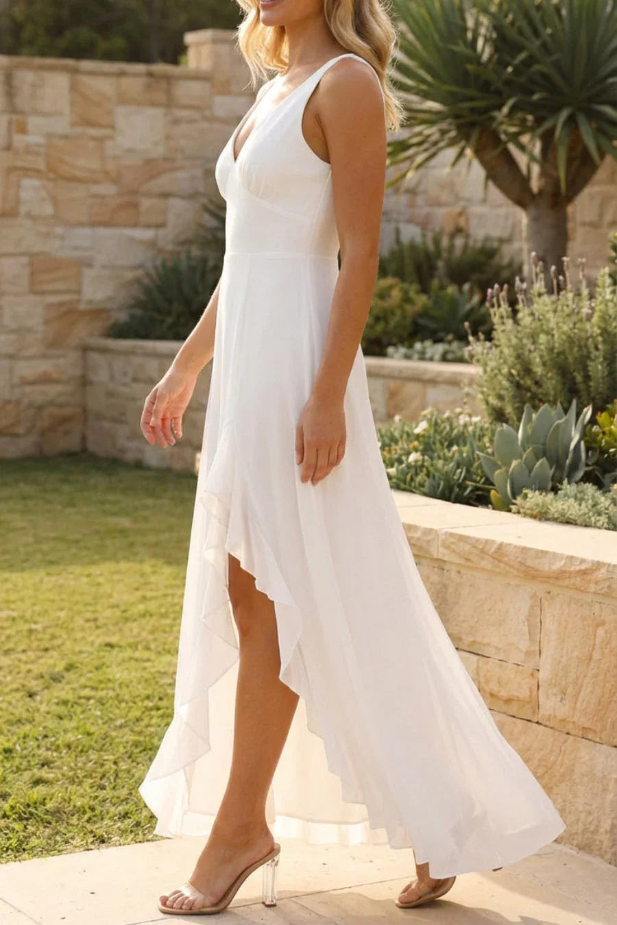 Woman in a white dress standing outdoors with a stone wall and plants in the background