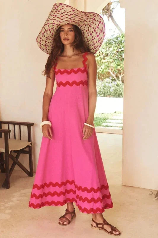 Woman wearing a pink dress with red trim and a large sun hat indoors.
