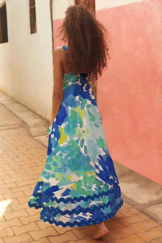 Woman in a blue floral dress standing against a pink wall.