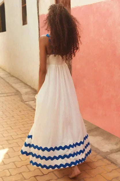 Woman in a white dress with blue trim walking down a street.