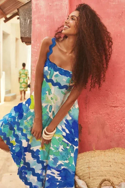 Woman in a colorful dress standing against a pink wall.