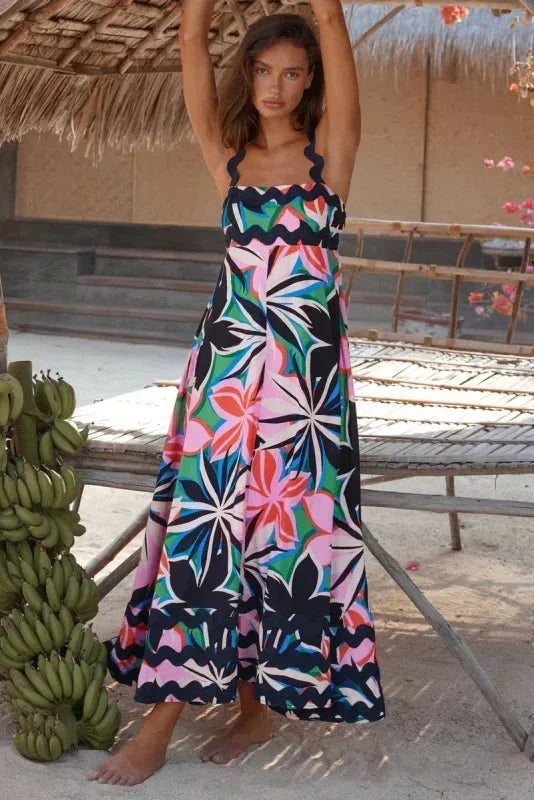 Woman in a colorful floral dress standing under a thatched roof with bananas nearby.