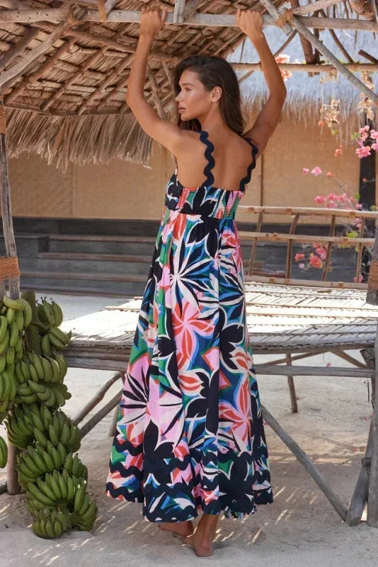 Woman in a colorful dress standing under a thatched roof with bananas and flowers in the background.