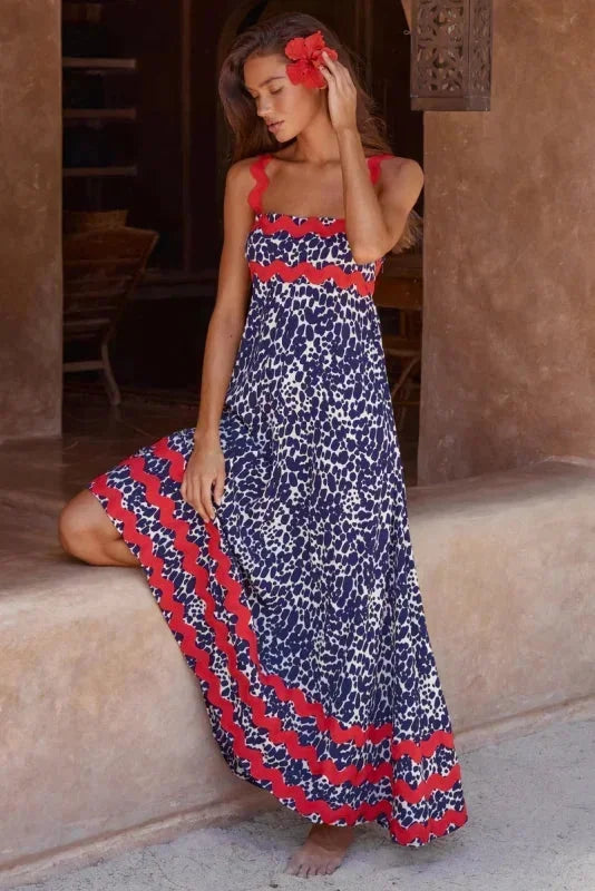 Woman wearing a blue and red patterned dress standing in a sunlit outdoor setting.