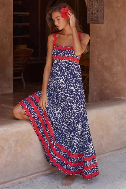 Woman wearing a blue and red patterned dress standing in a sunlit outdoor setting.