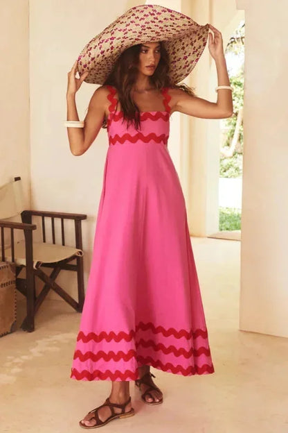 Woman wearing a pink dress with red trim and a large hat indoors.