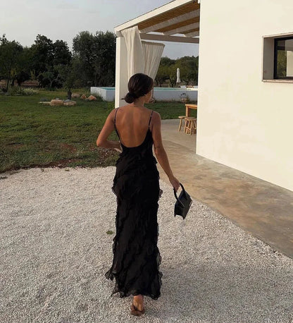 Woman in a black dress walking outdoors near a building with a pool.