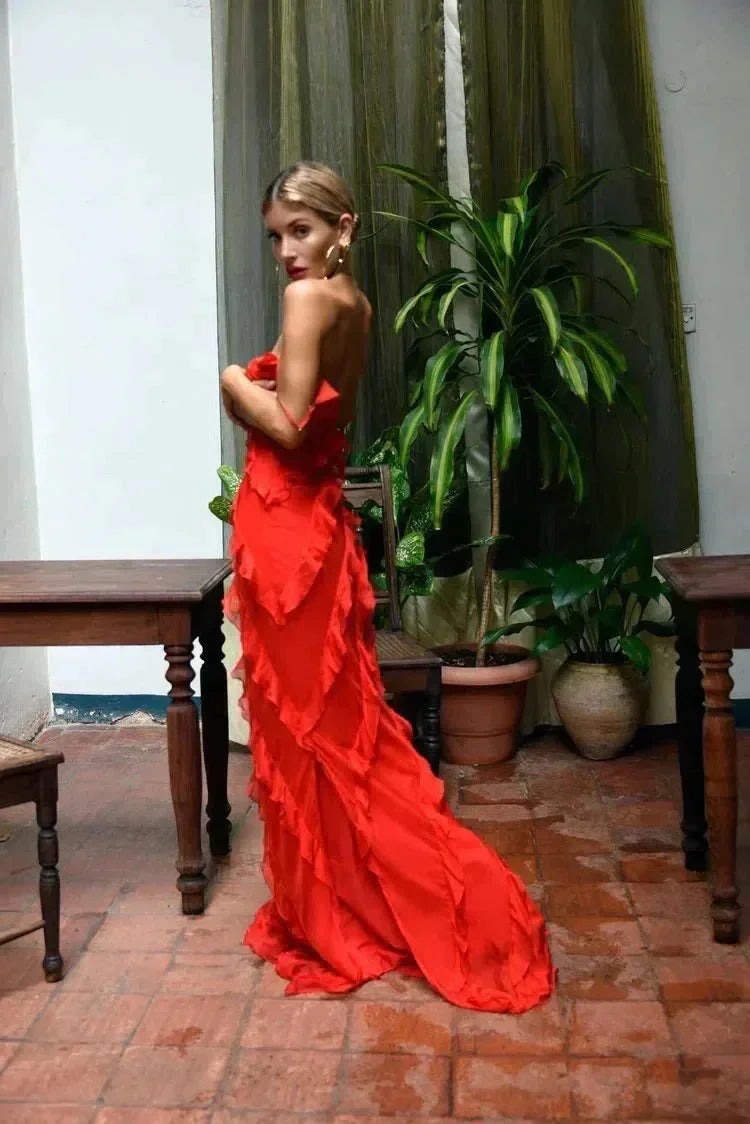 Woman in a red dress standing in a room with plants and wooden furniture.