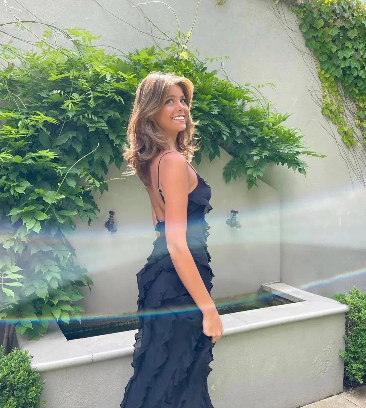 Woman in a dark blue dress standing outdoors with greenery in the background