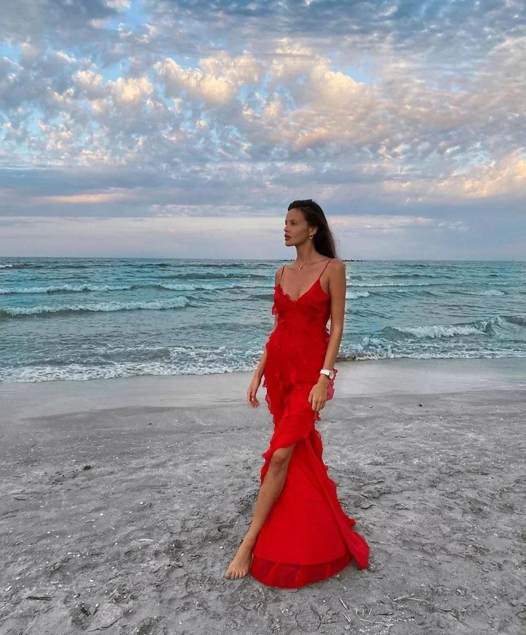 Woman in a red dress standing on a beach with ocean and sky in the background