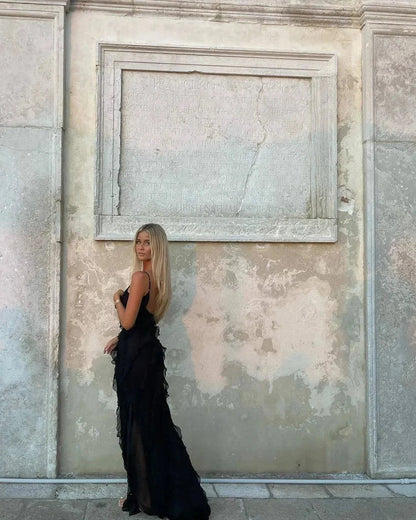 Woman in a black dress standing against a textured stone wall.