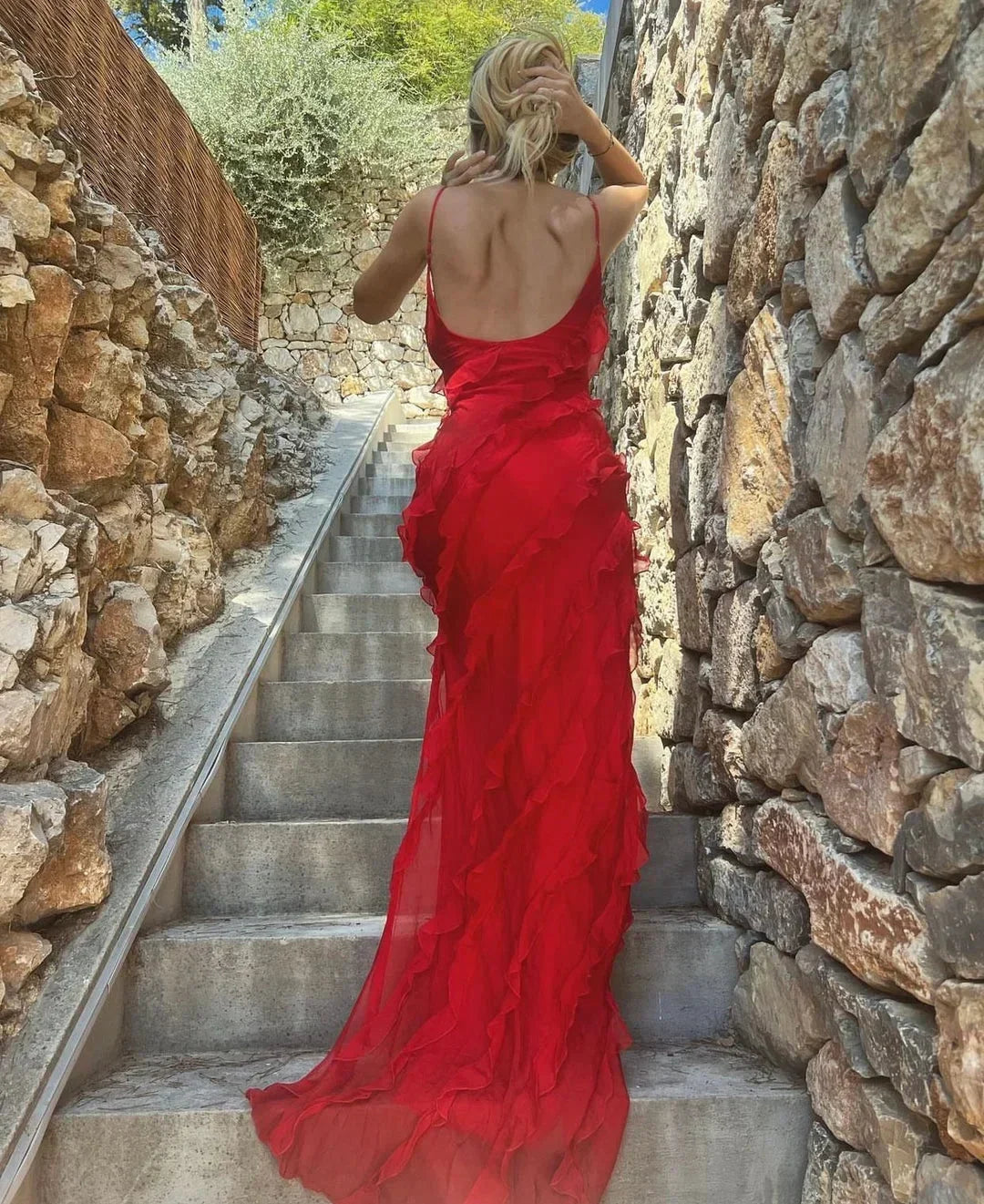 Woman in a red dress walking up stone steps in a sunlit outdoor setting