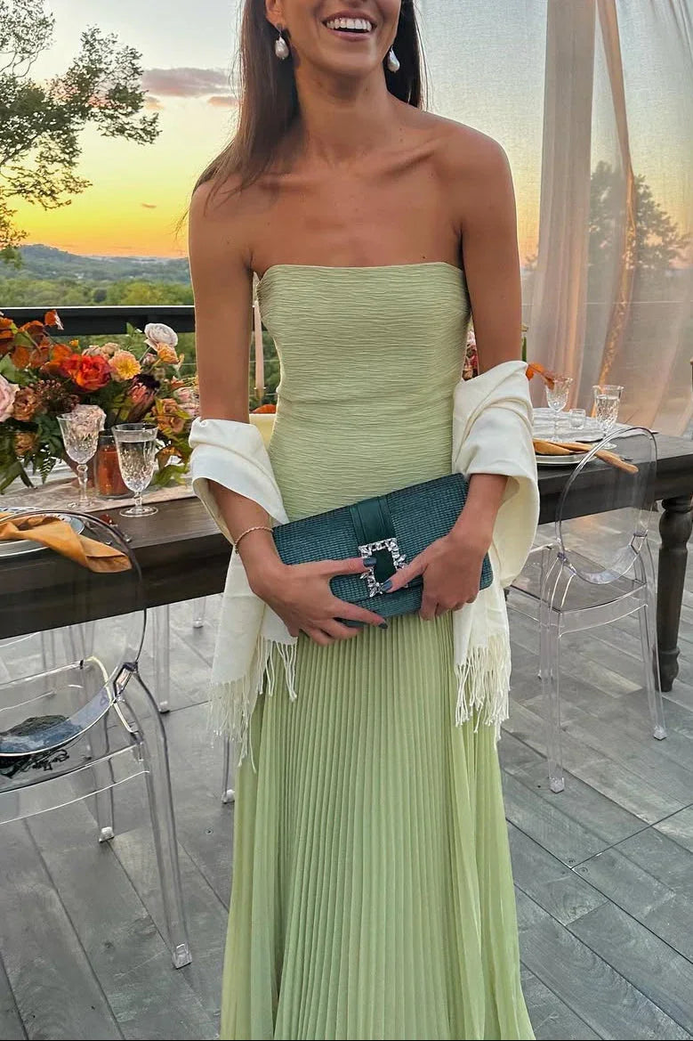 Woman in a strapless green dress holding a clutch at an outdoor event with a sunset view.