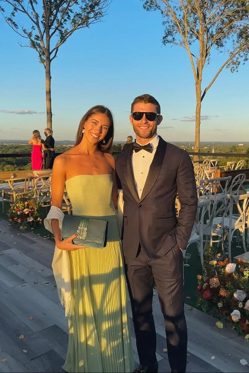 Man and woman posing outdoors in formal attire with a scenic background