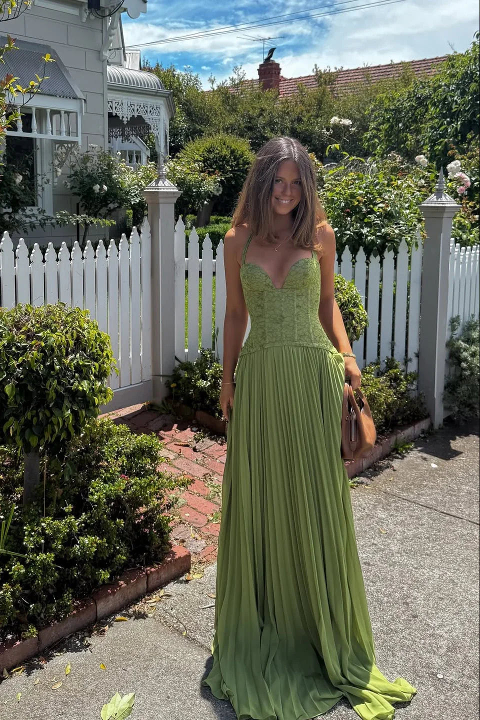 Woman in a green dress standing in a garden with a white picket fence.