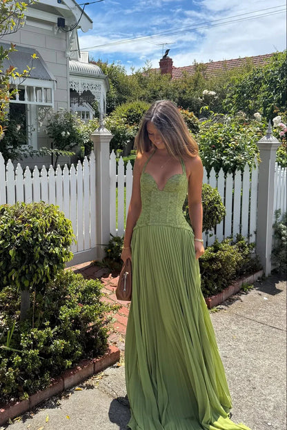 Woman in a green dress standing in a garden with a white picket fence and house in the background.