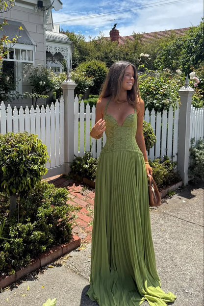 Woman in a green dress standing in a garden with a white picket fence.
