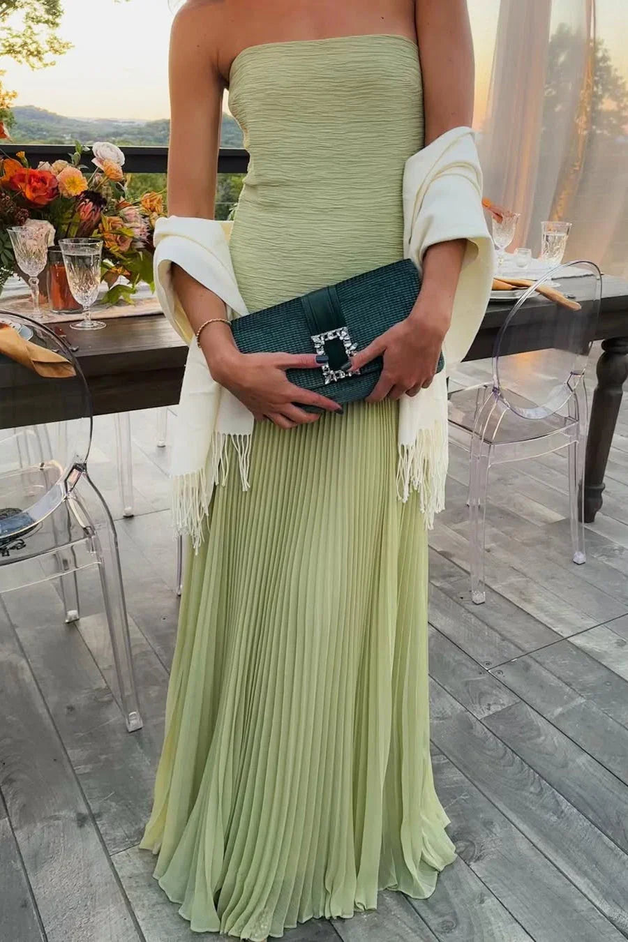 Woman in a green strapless dress holding a clutch outdoors.
