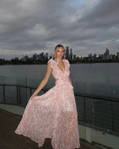 Woman in a pink floral dress standing on a balcony with a city skyline in the background