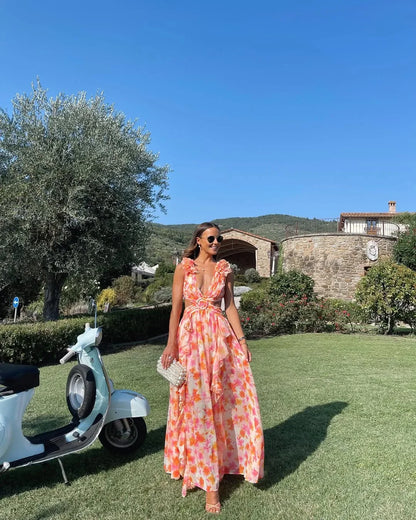 Woman in a colorful dress standing in a scenic outdoor setting with a scooter and stone building.