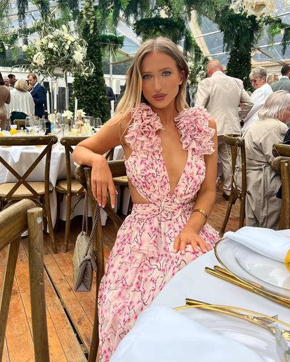 Woman in a pink floral dress at an outdoor event with tables and people in the background
