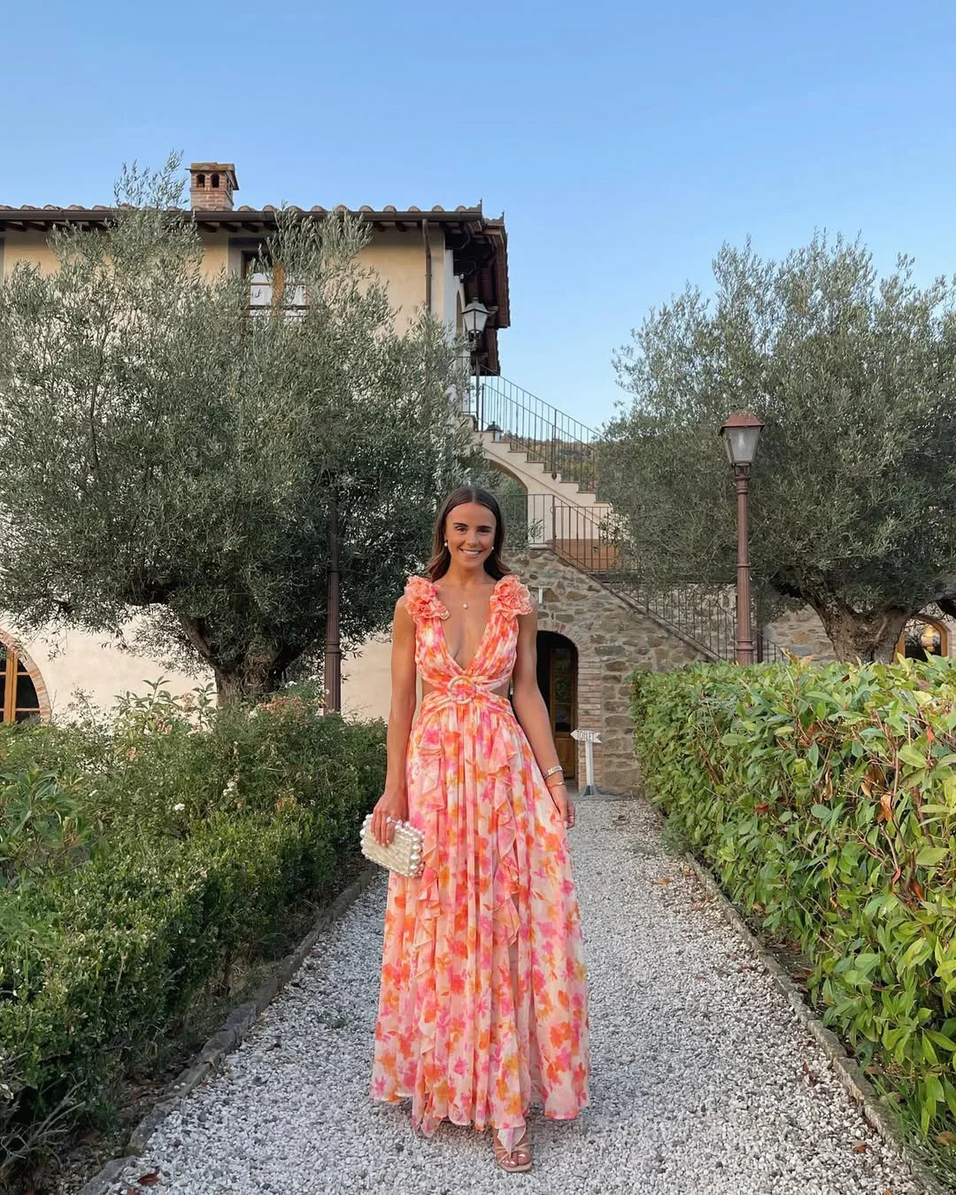 Woman in a floral dress standing on a gravel path with a villa in the background