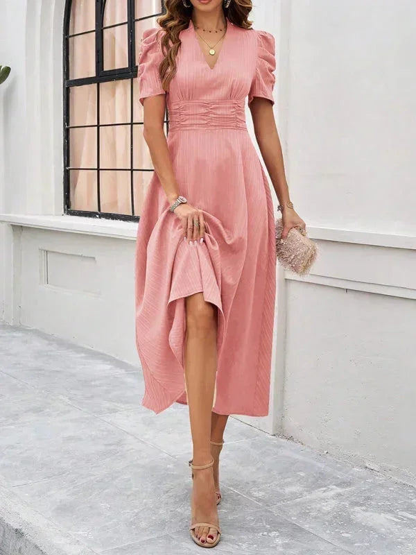 Woman wearing a pink dress standing in front of a white wall.