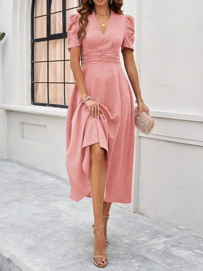 Woman wearing a pink dress standing in front of a white wall.