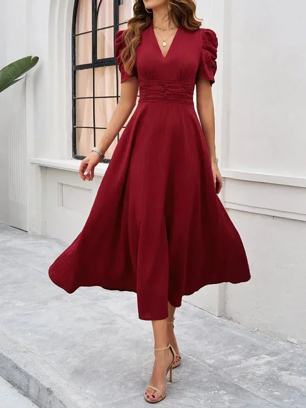 Woman wearing a red dress standing against a white wall.