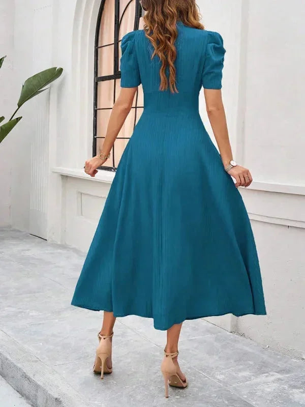 Woman wearing a teal dress standing in front of a white wall.
