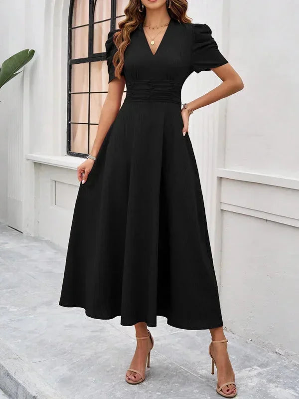 Woman wearing a black dress standing in front of a white wall.