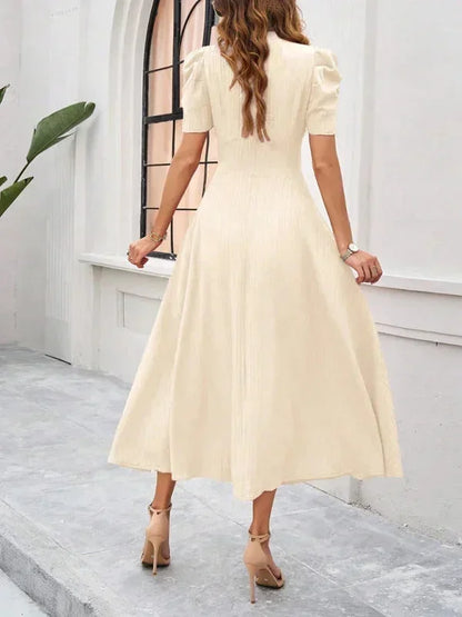 Woman wearing a beige dress standing in a room with white walls and a window.