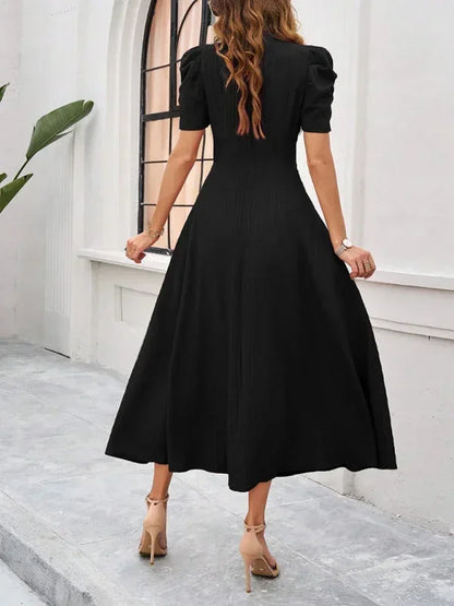 Woman wearing a black dress standing in front of a white wall.