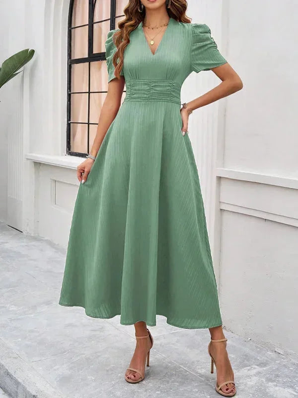 Woman wearing a green dress standing against a white wall.