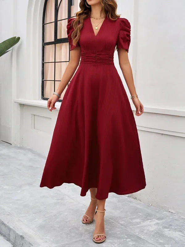 Woman wearing a burgundy dress standing in front of a white wall.