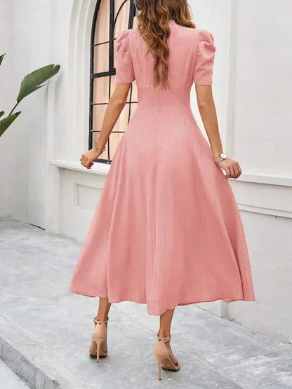 Woman wearing a pink dress standing in front of a white wall.