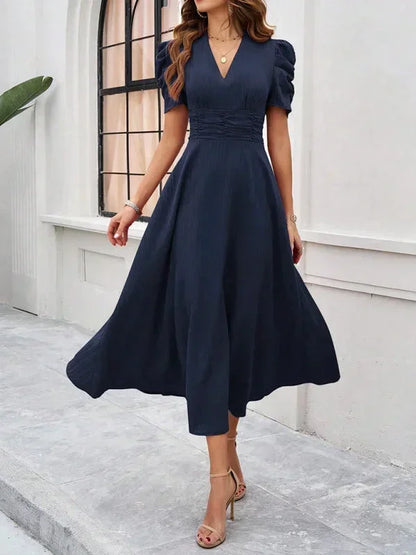 Woman wearing a navy blue dress standing in front of a white wall.