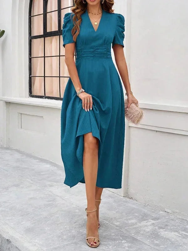 Woman wearing a teal dress with puff sleeves in an outdoor setting.