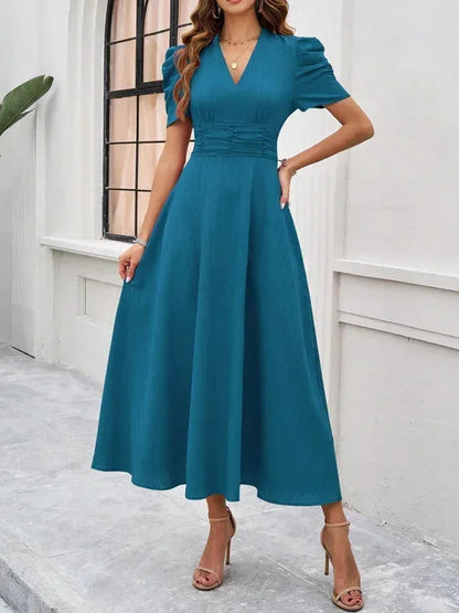 Woman wearing a teal dress standing against a white wall.
