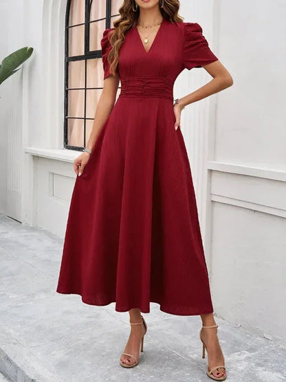 Woman wearing a burgundy dress standing against a white wall.