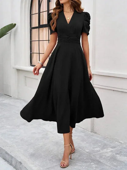 Woman wearing a black dress standing in front of a white wall.