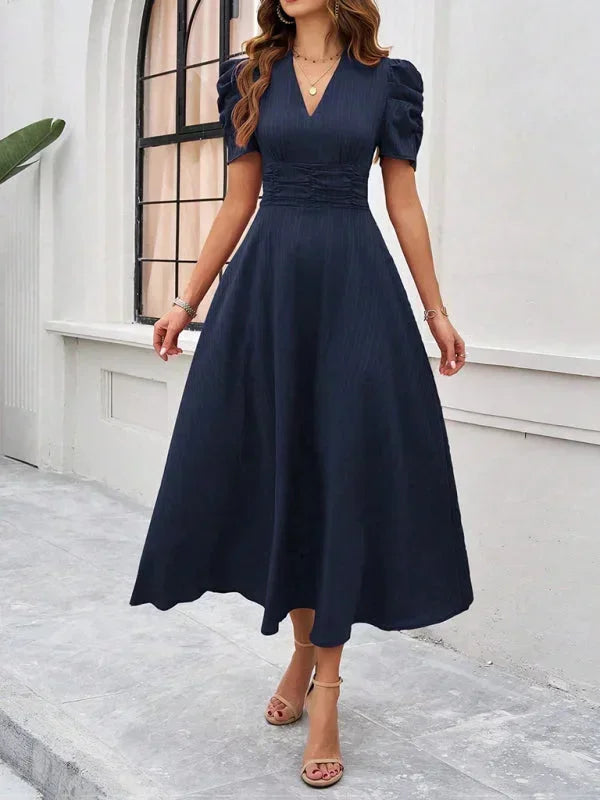 Woman wearing a black dress standing in front of a white wall.