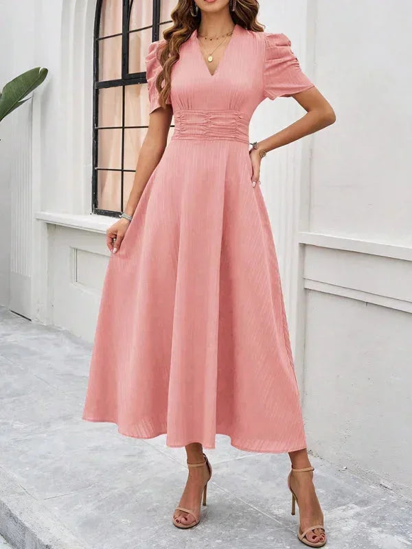Woman wearing a pink dress standing against a white wall.
