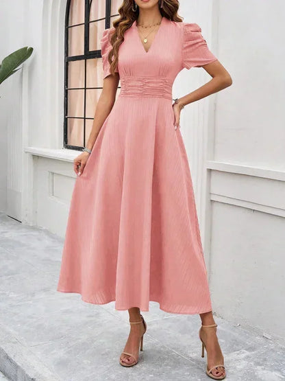 Woman wearing a pink dress standing against a white wall.