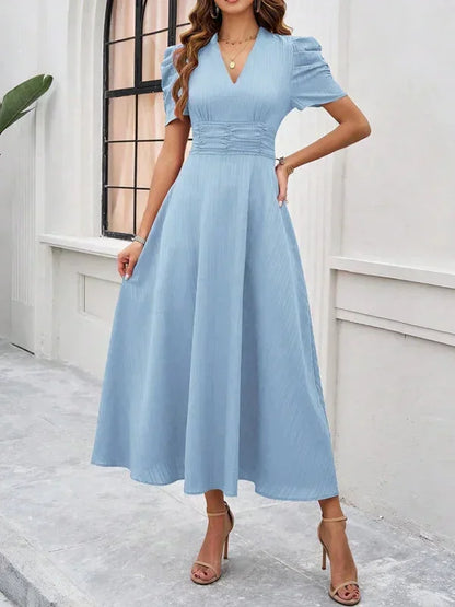 Woman wearing a light blue dress standing against a white wall.