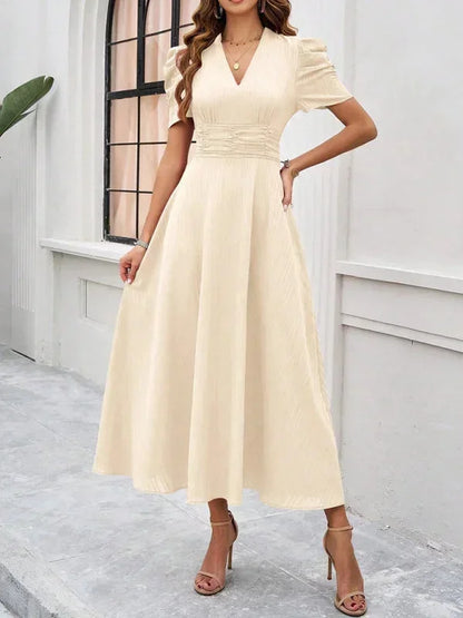 Woman wearing a beige dress standing in front of a white wall.